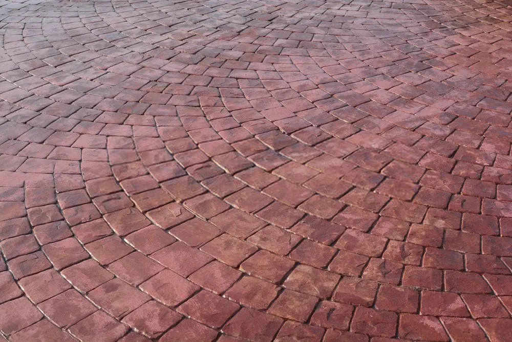A surface covered with reddish-brown cobblestones arranged in a circular pattern, creating a textured and visually appealing design. The stones vary slightly in shade and tone, adding depth to the overall appearance. For those in Coral Gables FL seeking similar designs, get your free service quote for decorative concrete today!